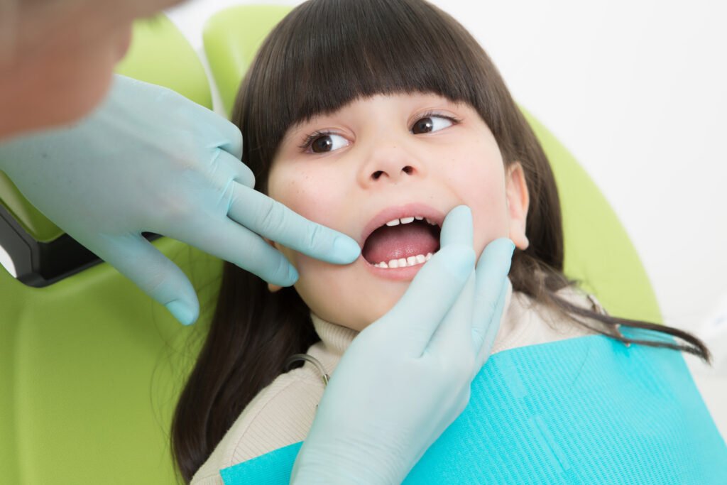 A dentist is examining the teeth of a young child in a dental chair.