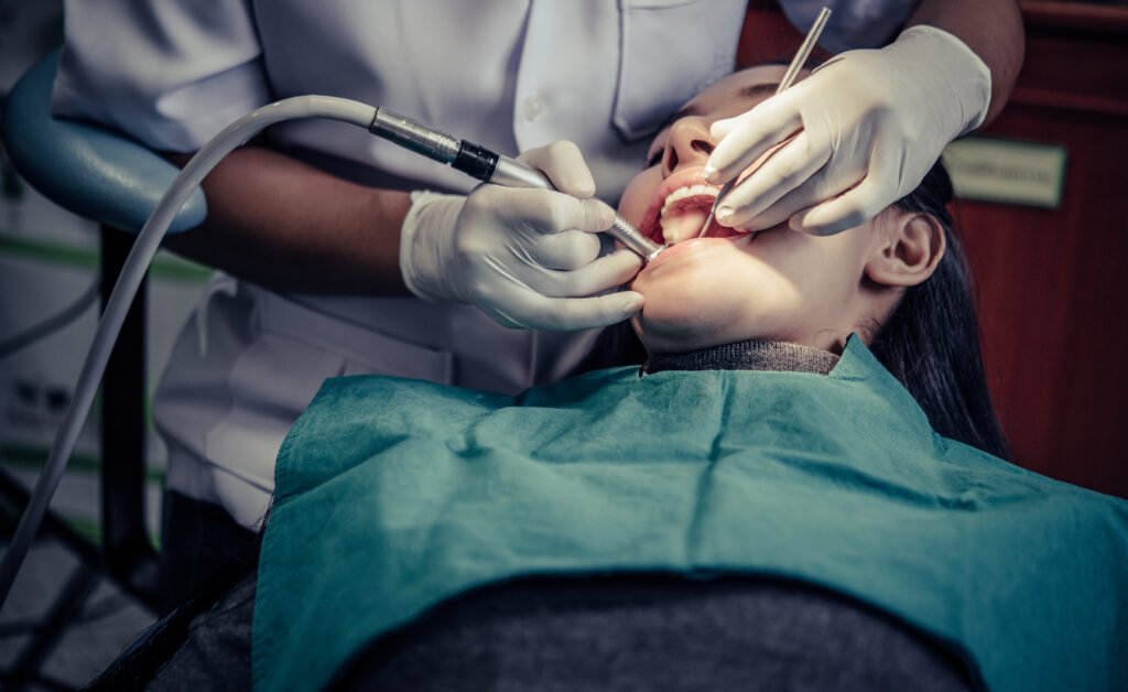 A dentist is performing a procedure on a patient using a dental drill and other tools in a clinic.