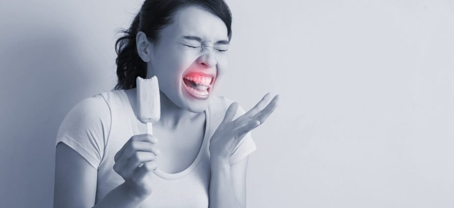 A woman wincing in pain after eating something cold, holding an ice cream while experiencing tooth sensitivity or pain.