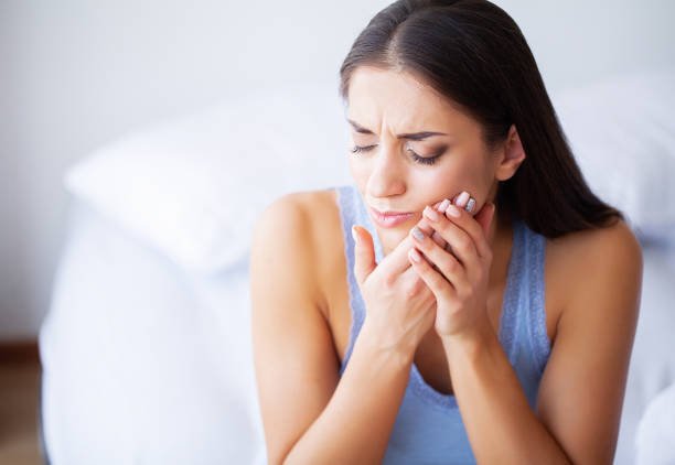 A woman is holding her jaw with a pained expression, possibly experiencing tooth or jaw pain.