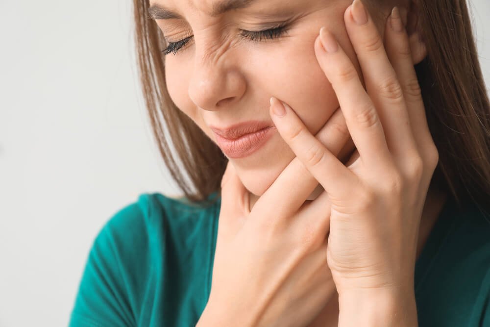 Young woman experiencing tooth pain, holding her jaw in discomfort.
